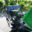 Vue rapprochée du poste de commande et du moteur d’un mini dumper à chenilles, avec leviers de contrôle et benne partiellement levée