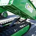 Zoom sur le système hydraulique de levage d’un mini dumper à chenilles vert, benne relevée avec vérin et chenilles caoutchouc apparentes, logo ChargeurPlus