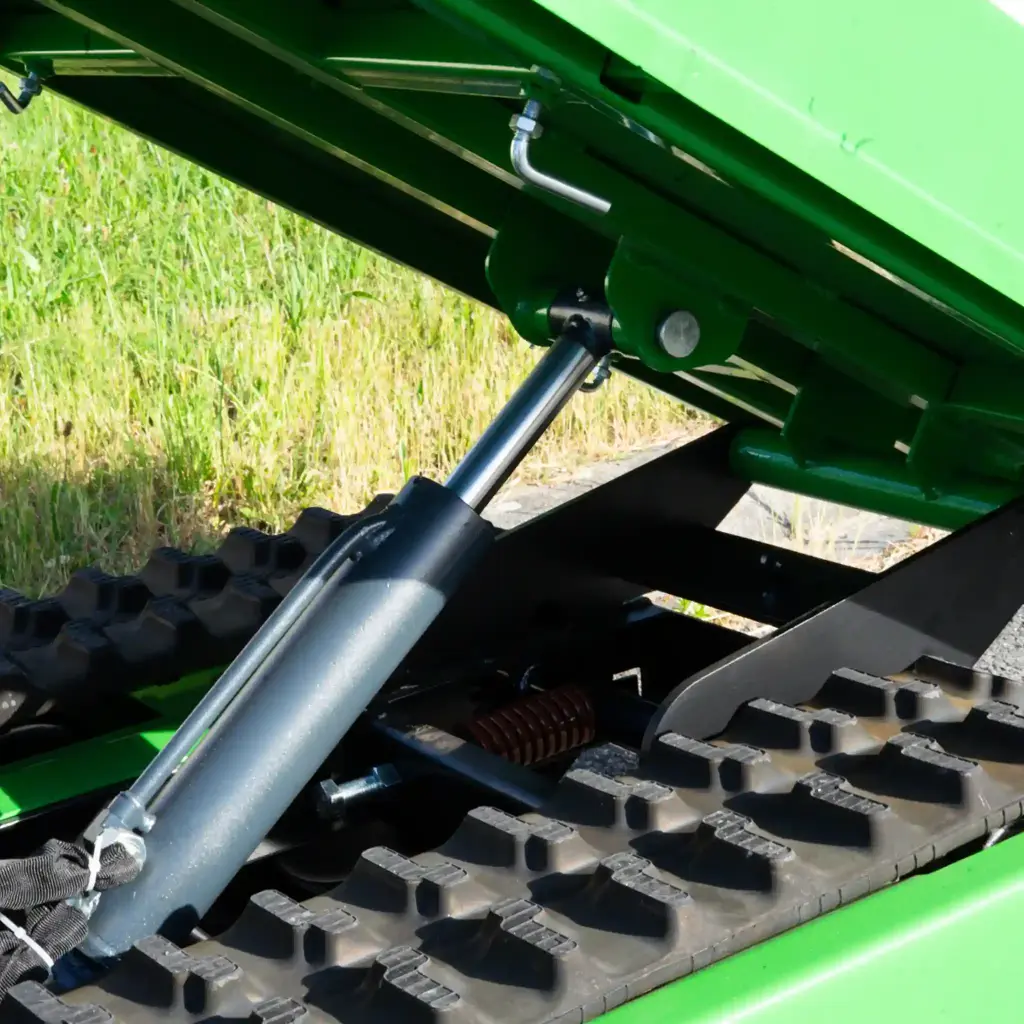 Zoom sur le vérin hydraulique de levage d’un mini dumper à chenilles, benne en position inclinée et chenilles visibles