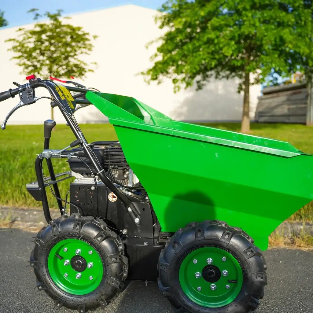 Mini dumper motorisé vert à quatre roues, benne en position horizontale et manettes de contrôles, stationné en extérieur sur un sol sur la route avec fond d'arbres
