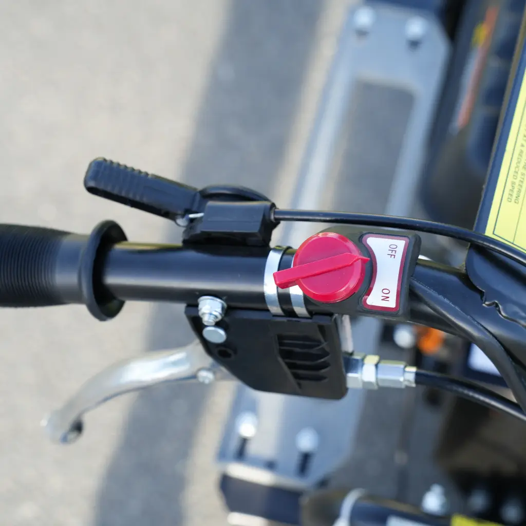 Gros plan sur la poignée de commande d’un mini dumper, avec interrupteur rotatif rouge ON/OFF et levier de frein