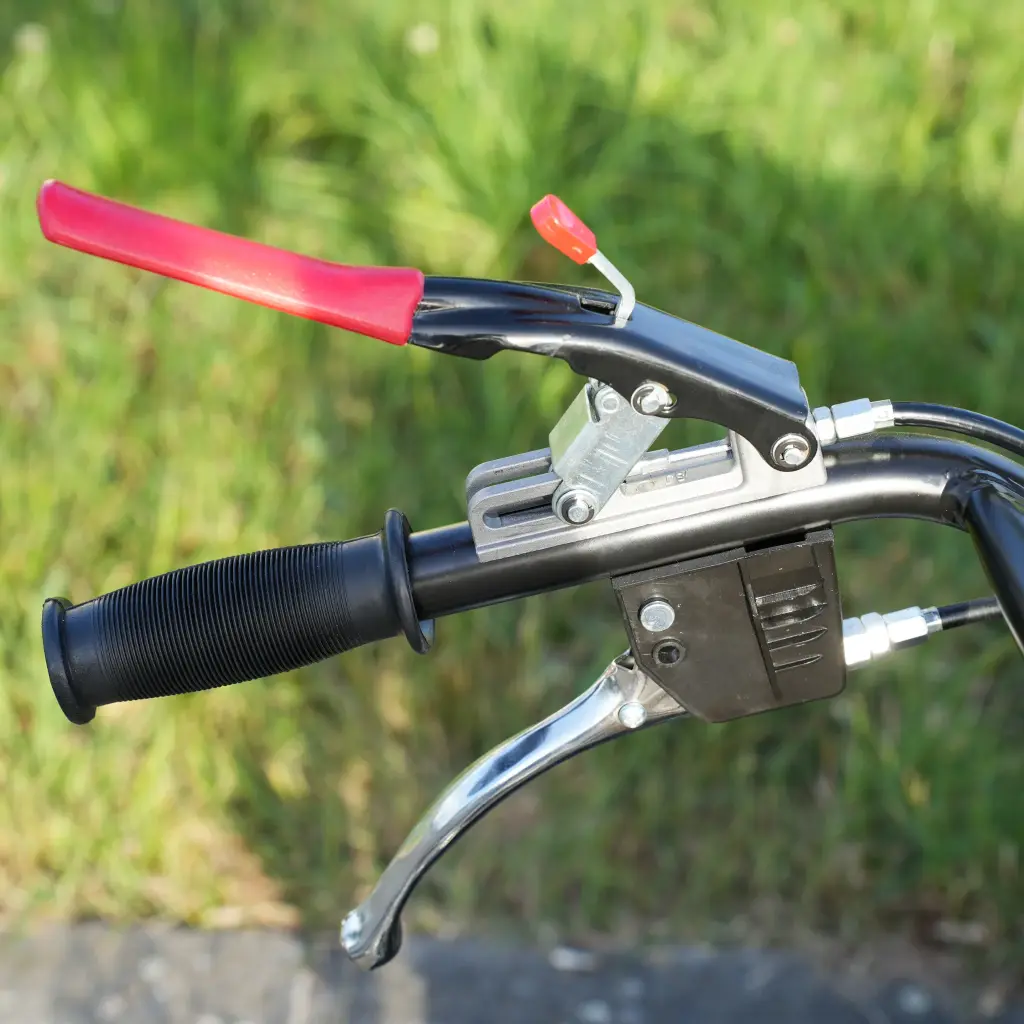 Zoom sur la poignée gauche d’un mini dumper avec levier de frein rouge, commande de sécurité et poignée