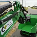 Zoom sur le bras articulé hydraulique d’une mini-pelle verte Chargeur Plus, avec flexibles gainés, vérins et godet avant, vue extérieure sur route