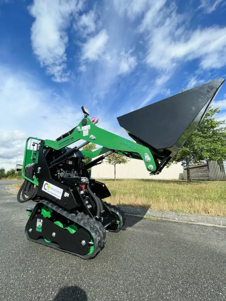 mini chargeuse mc306 de chez chargeur plus avec un godet à fond plat de 130L sur la route avec un ciel bleu.webp