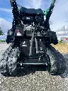 vue en contre plongée des chenilles d'une mini pelle mc306 de chez chargeur plus sur une route avec un fond de ciel bleu.webp