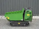 Vue latérale d’un mini dumper vert à chenilles, avec benne basculante, moteur caréné et pictogrammes de sécurité visibles sur fond de mur gris.