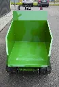 Benne vide d’un dumper à chenilles vert vue de face, avec commandes de pilotage visibles à l’arrière et sol bitumé en arrière-plan.