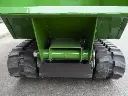 Vue arrière d’un dumper à chenilles vert, centrée sur le châssis et la fixation de la benne, avec les chenilles caoutchouc en contact avec le sol bitumé.