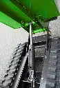 Vérin hydraulique d’un dumper à chenilles vert en position de levage, visible entre les chenilles caoutchouc sur sol asphalté.