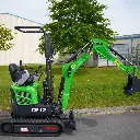 photo de côté d'une mini-pelle CP12 sur un terrain en fond, on apperçoit sur la photo les chenilles de la mini-pelle, les manettes, et un godet au bout du bras de la flèche. Le vérin est inversé