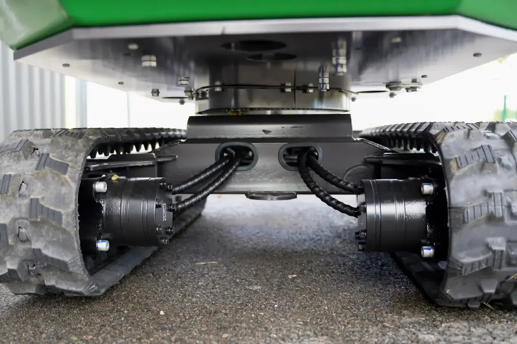 Chargeurplus: Vue détaillée du train de roulement sur chenilles, mettant en valeur les moteurs hydrauliques, les raccordements renforcés et la structure robuste assurant stabilité et mobilité sur tous types de terrains.