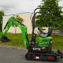 photo de profil d'une mini-pelle CP12 avec un fond en ciel bleu, on apperçoit sur la photo les chenilles de la mini-pelle, les manettes, et un godet au bout du bras de la flèche. Le vérin est inversé