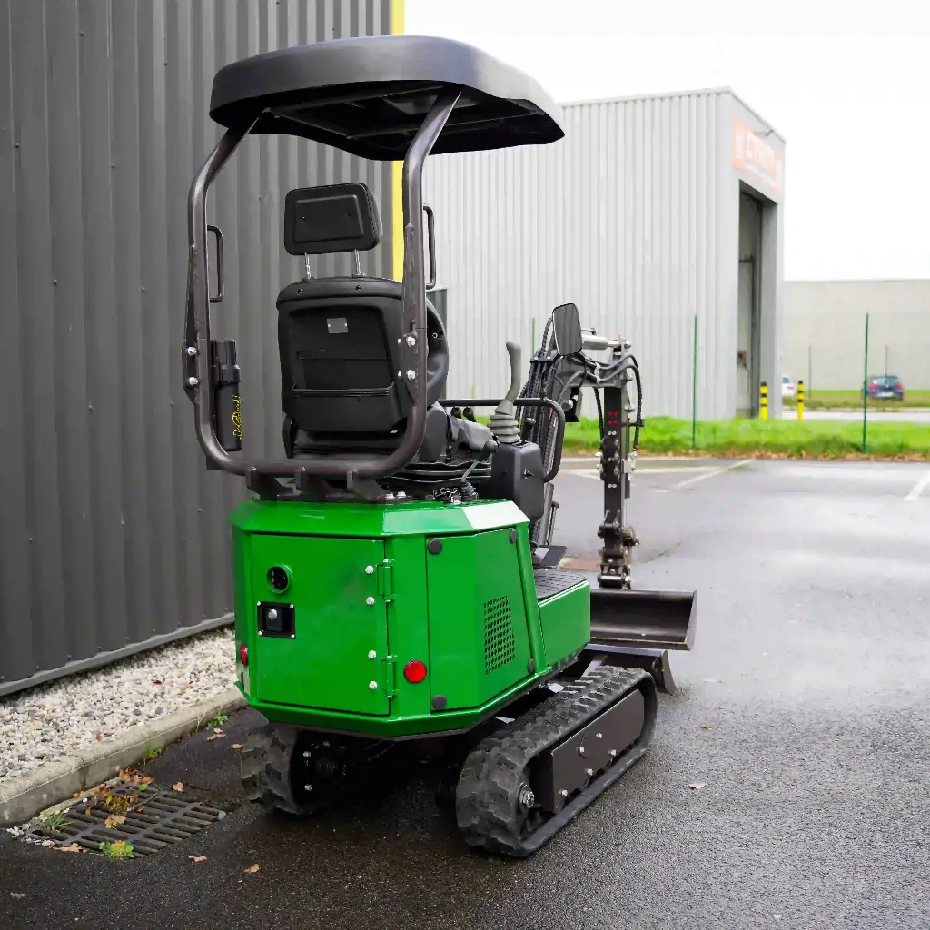 Chargeurplus vous présente la même mini-pelle verte sur chenilles, cette fois photographiée de trois quarts arrière gauche, révélant le dossier du siège opérateur, la structure du ROPS et la partie arrière de la carrosserie verte avec le bras hydraulique replié visible sur le côté droit.