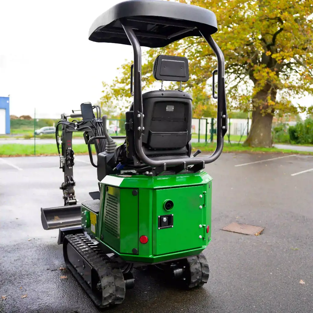 Chargeurplus vous présente la mini-pelle verte photographiée de l'arrière, mettant en valeur la carrosserie verte avec ses trappes d'accès, le bouton d'arrêt d'urgence rouge, le siège et la structure ROPS, avec le bras hydraulique et le godet visibles sur la gauche.
