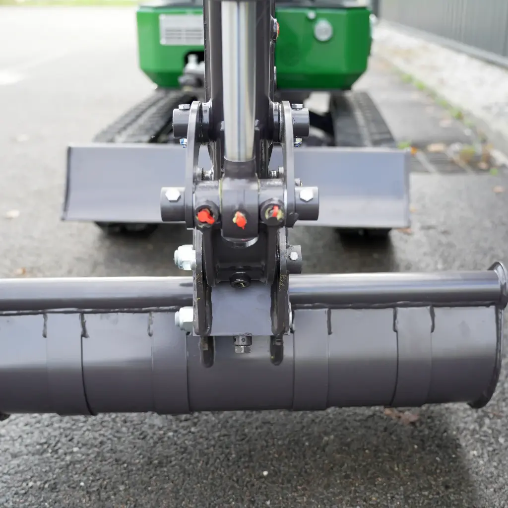 Chargeurplus vous présente un gros plan sur l'attache rapide de la CP09, montrant le système de verrouillage avec ses deux goupilles de sécurité rouges et oranges, ainsi que le godet cylindrique interchangeable monté en position basse.