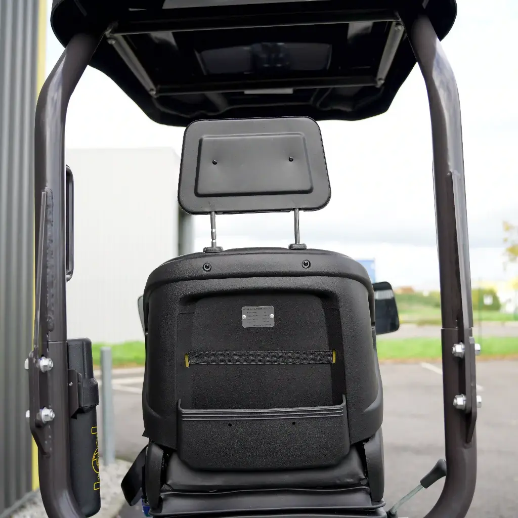 Chargeurplus vous présente un gros plan sur le siège opérateur de la CP09, montrant le dossier rembourré avec appuie-tête réglable, la ceinture de sécurité jaune et la plaque signalétique, encadré par la structure ROPS et l'auvent de protection.