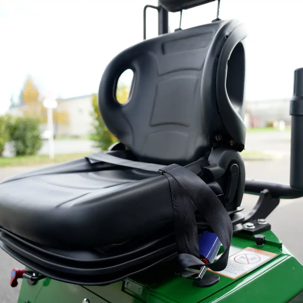 Chargeurplus vous présente un gros plan sur le siège opérateur de la CP09 vu de trois quarts, mettant en valeur l'assise en similicuir noir, le dossier ergonomique avec poignée de maintien et la ceinture de sécurité, sur fond de paysage extérieur flou.