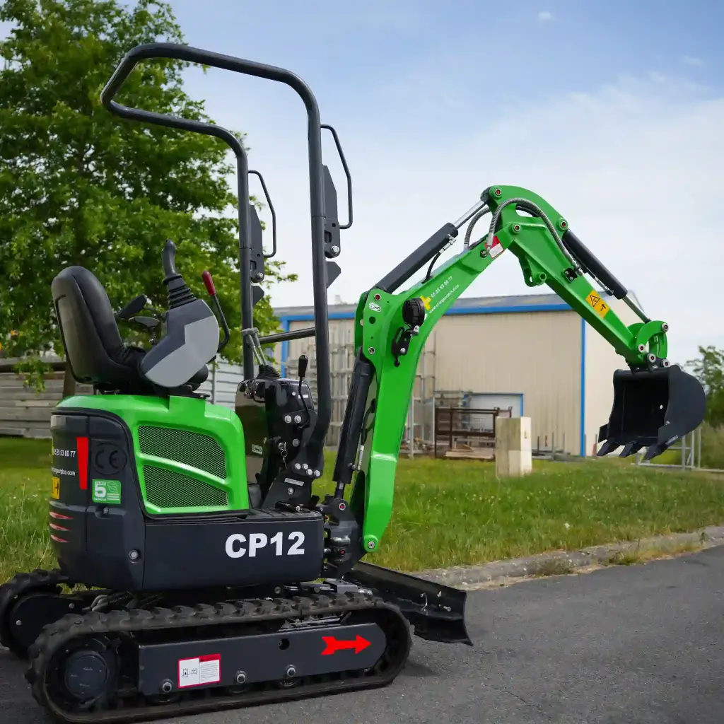 photo de profil d'une mini-pelle CP12 avec un fond en ciel bleu, on apperçoit sur la photo les chenilles de la mini-pelle, les manettes, et un godet ou bout du bras de la flèche. Le vérin est inversé
