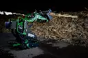 Chargeurplus vous présente le mini chargeur sur chenilles équipé d'un grappin, soulevant des planches de bois devant un important tas de chutes de bois dans un…Chargeurplus vous présente le mini chargeur sur chenilles équipé d'un grappin, soulevant des planches de bois devant un important tas de chutes de bois dans un hangar, démontrant sa polyvalence pour la manutention de matériaux encombrants en espace intérieur.