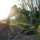 Chargeurplus vous présente le mini chargeur sur chenilles en pleine action au coucher du soleil, bras levé au maximum déversant de la terre et des gravats, conduit par un opérateur en sweat Chargeurplus, dans une atmosphère lumineuse et dynamique qui met en valeur la puissance de la machine.