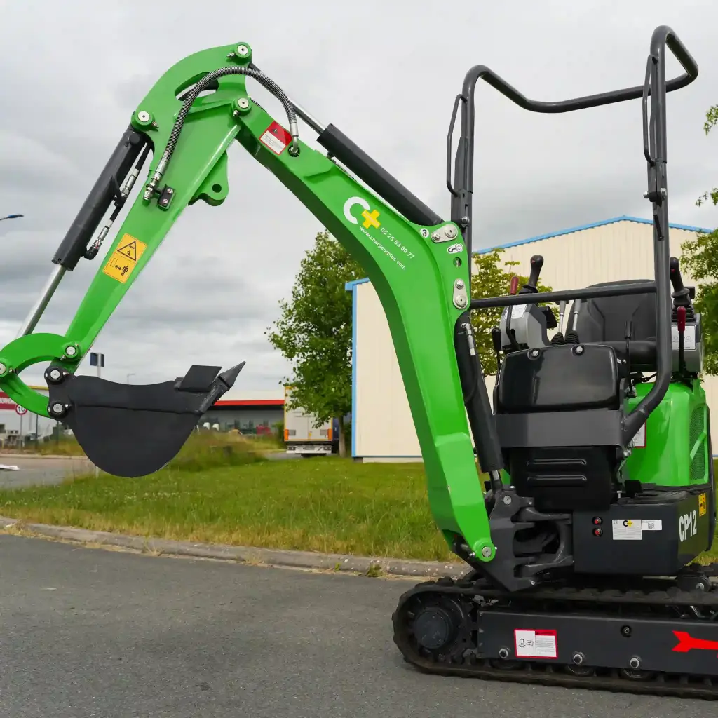 vue en contre-plongée d'une mini-pelle cp12 1200kg avec le déport de flèche intégré et un vérin inversé, la pelle est sur un terrain.
