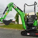 vue en contre-plongée d'une mini-pelle cp12 1200kg avec le déport de flèche intégré et un vérin inversé, la pelle est sur un terrain.