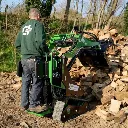 Chargeurplus vous présente le mini chargeur sur chenilles équipé d'un grappin en train de manipuler des bûches de bois de chauffage, conduit debout par un opérateur en sweat Chargeurplus, illustrant parfaitement son efficacité pour la gestion de bois en extérieur.