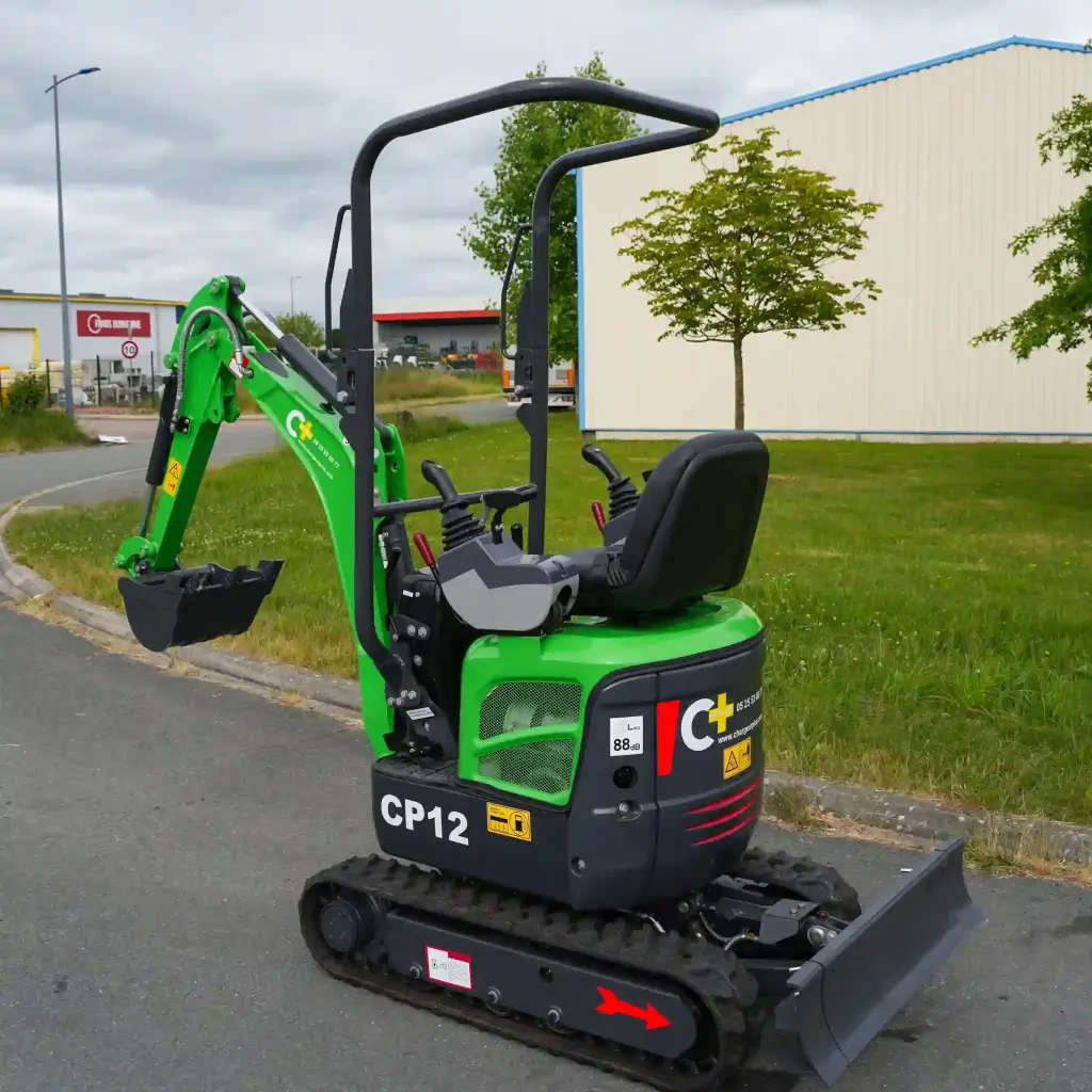 photo de derrière d'une mini-pelle CP12 avec sur un terrain, on aperçoit sur la photo les chenilles de la mini-pelle, les manettes, et un godet ou bout du bras de la flèche. Le vérin est inversé