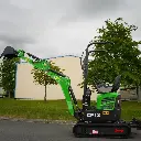 photo de côté d'une mini-pelle CP12 sur une route, on aperçoit sur la photo les chenilles de la mini-pelle, les manettes, et un godet au bout du bras de la flèche. Le vérin est inversé. Le bras est étendu à sa hauteur maximale