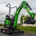 photo de côté d'une mini-pelle CP12 sur une route, on aperçoit sur la photo les chenilles de la mini-pelle, les manettes, et un godet au bout du bras de la flèche. Le vérin est inversé