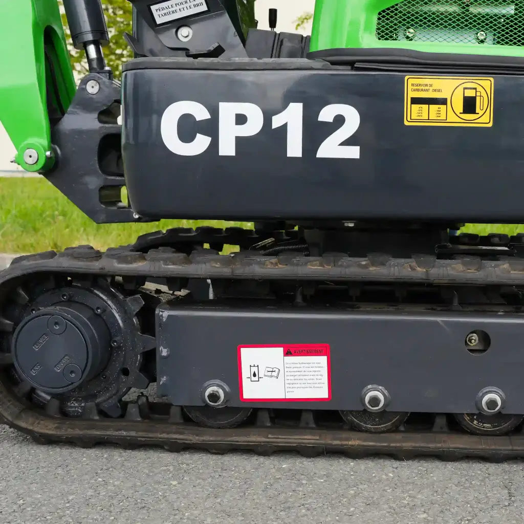 photo de côté des chenilles de la CP12, avec notice de sécurité et notice de consommation d'essence visbibles. Gamme de CP12 écrit en gros en blanc