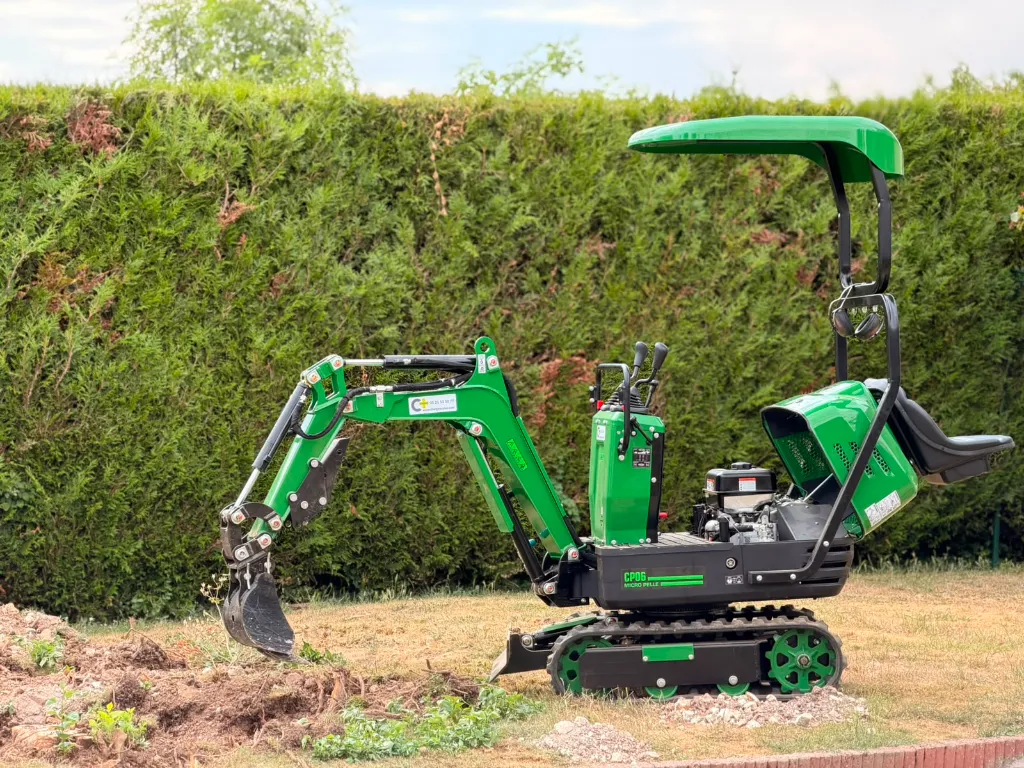 Vue de profil de la mini-pelle CP06 Chargeur Plus en intervention sur un chantier de dessouchage résidentiel.