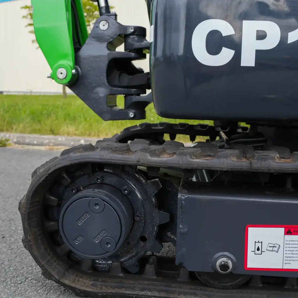 zoom de côté sur les extrémités des chenilles. Roues crampés et moteur d'avancement visible, avec notice de sécurité sur l'utilisation du moteur d'avancement.