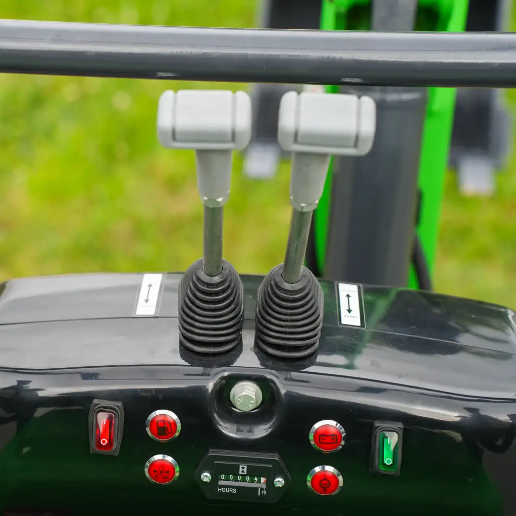 vue de haut et de face des manettes de commande de la mini-pelle. Boutons essence et batterie en rouge visibles.