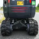 zoom de dos sur les chenilles de la mini-pelle. Chenilles étendues au minimum. Notice de sécurité en jaune visible.